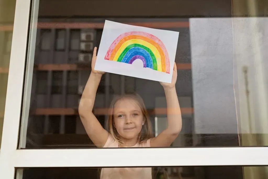 Little girl holding up rainbow she painted during coronavirus pandemic.
