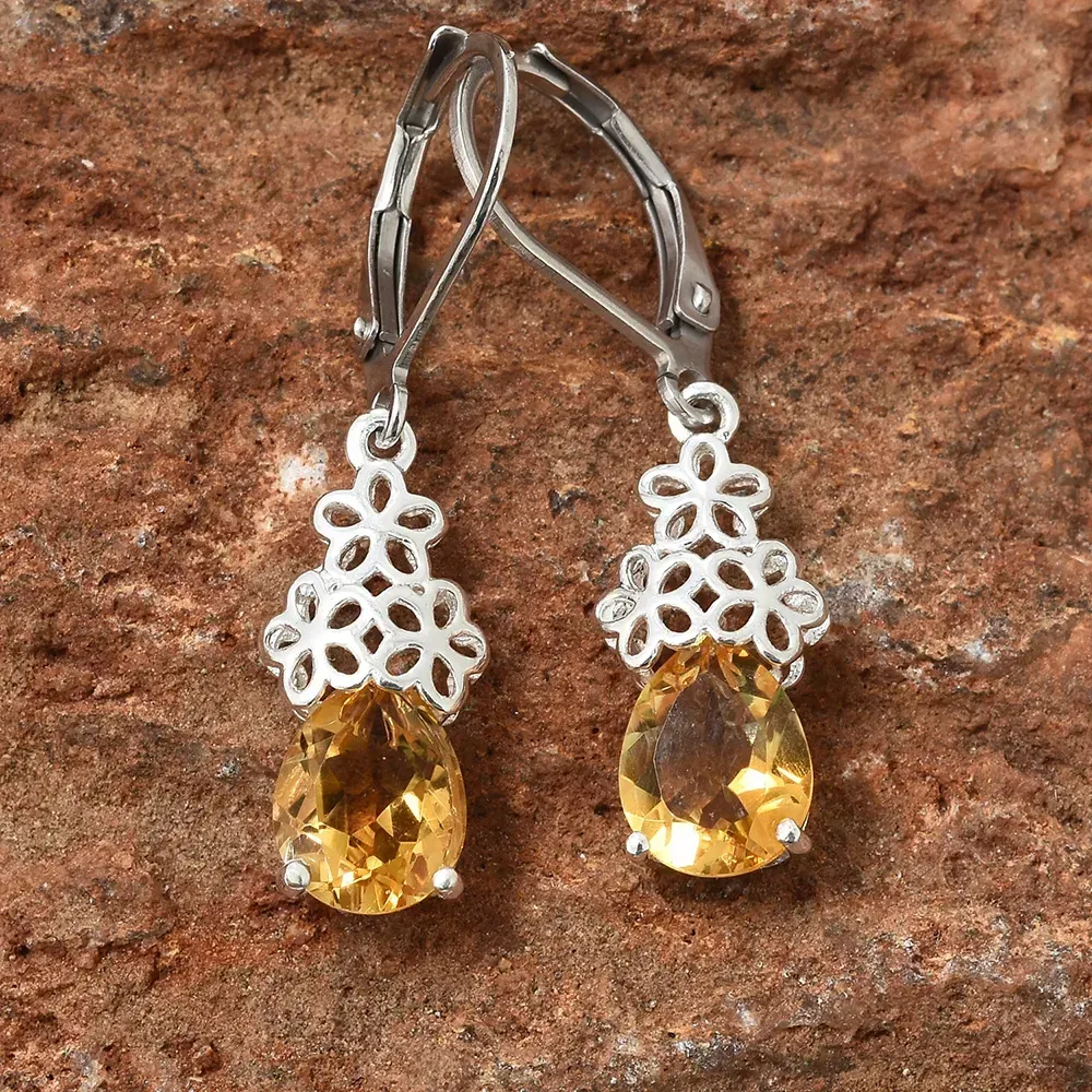Pair of dangle citrine earrings with metal lace detail against brown marble.