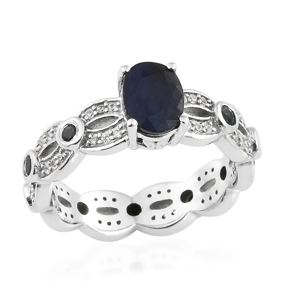 Closeup of blue sapphire ring with silver band against white background.