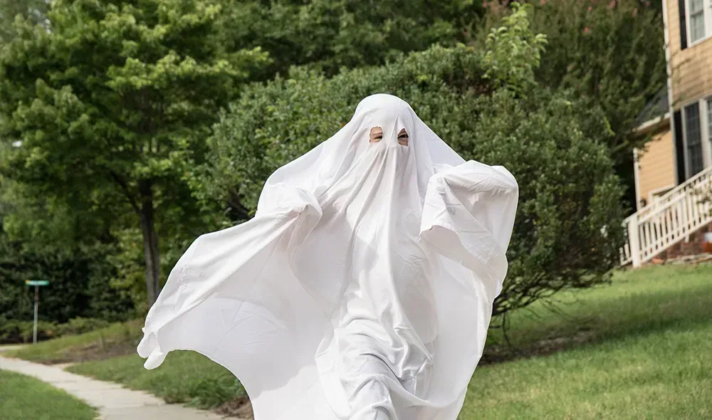 Kid running down the neighborhood dressed as a ghost