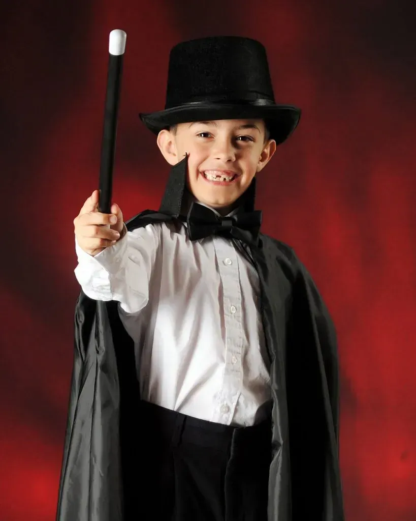 Kid dressed as a magician in front of red curtain