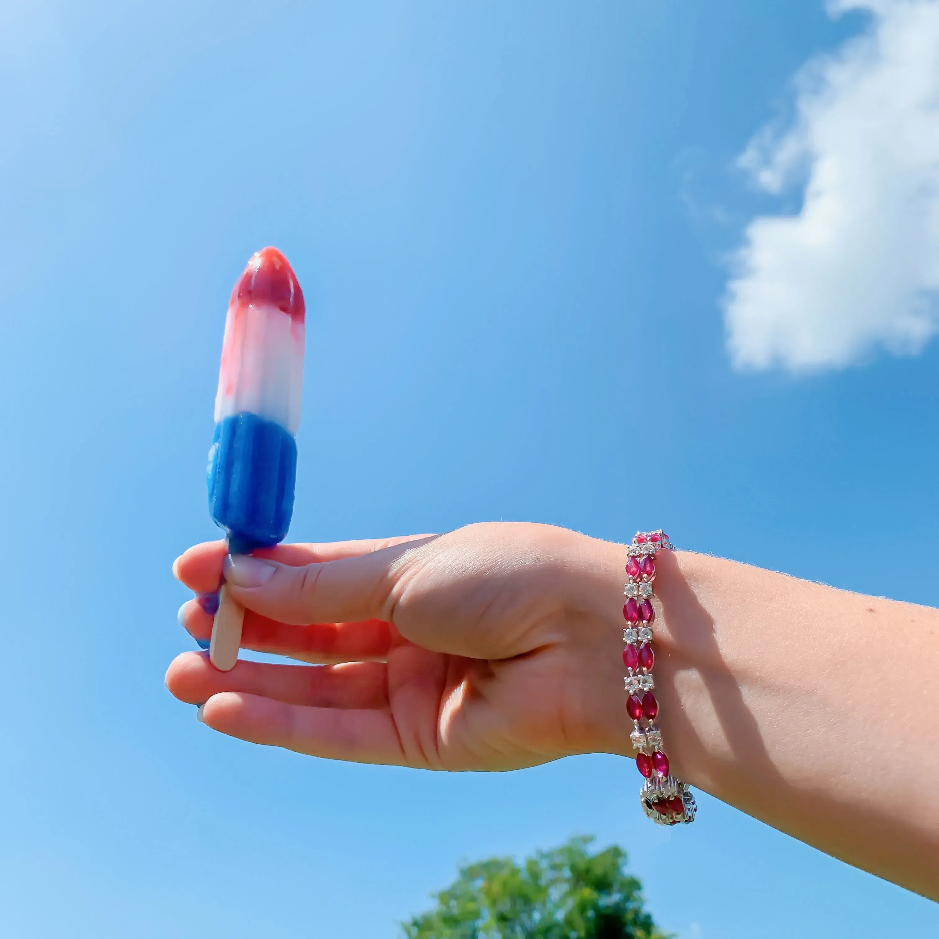 Woman's hand holding a popsicle against a clear sky. 