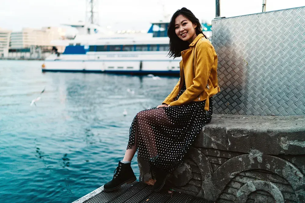 Woman sitting in the pier with her maxi dress, a yellow jacket and black ankle boots