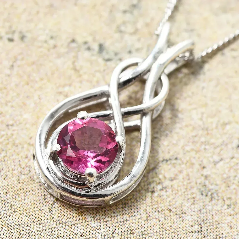 Closeup of pink gem pendant set in silver against brown marble counter