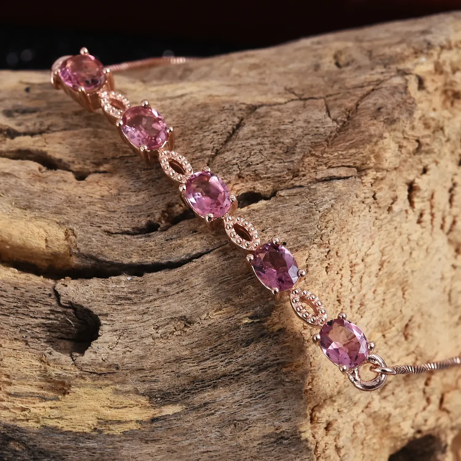 Pink tourmaline bracelet laying over driftwood.