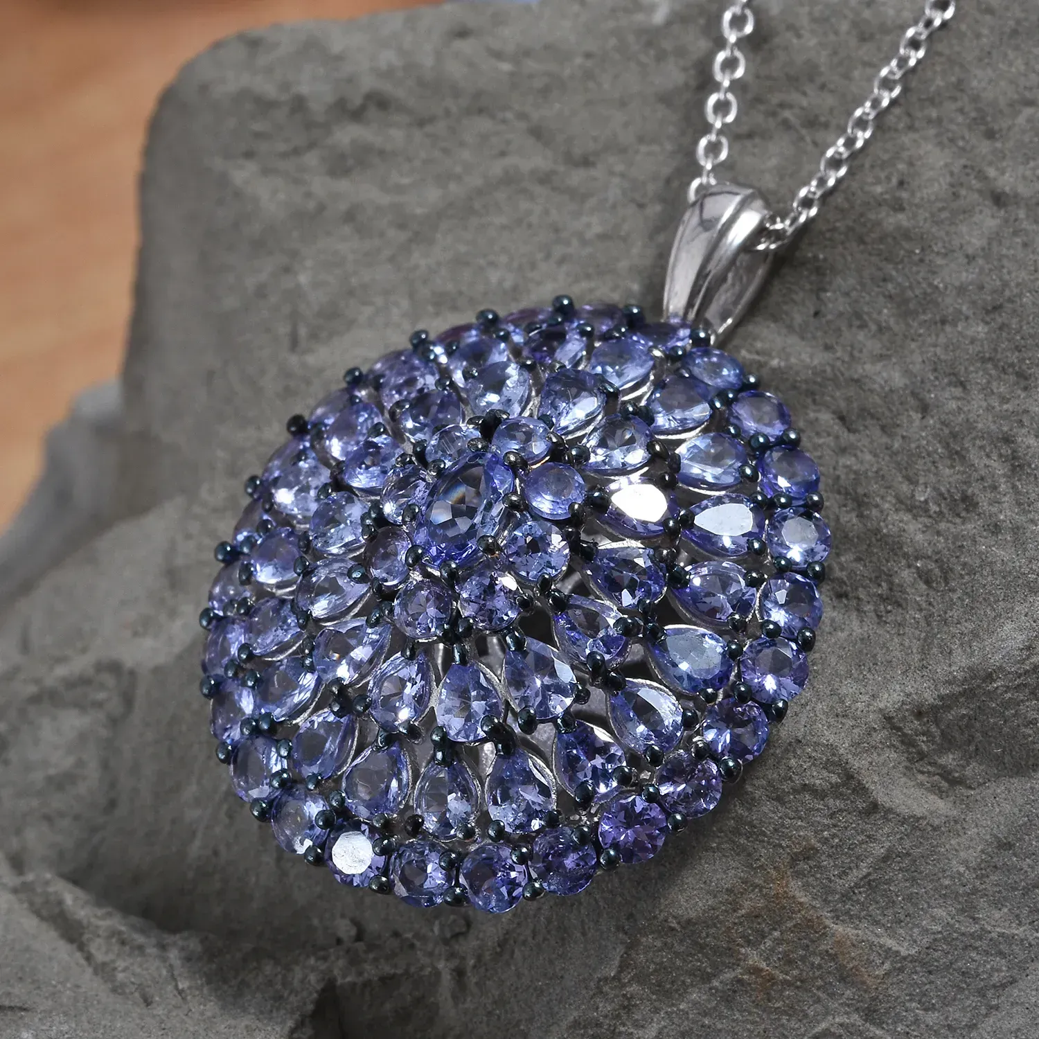 Blue tanzanite burst pendant draped over rock. 