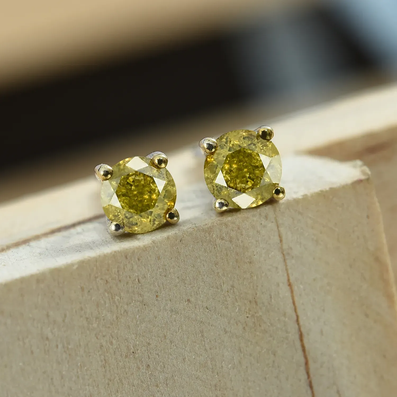 Yellow diamond stud earrings displayed on wooden plinth.