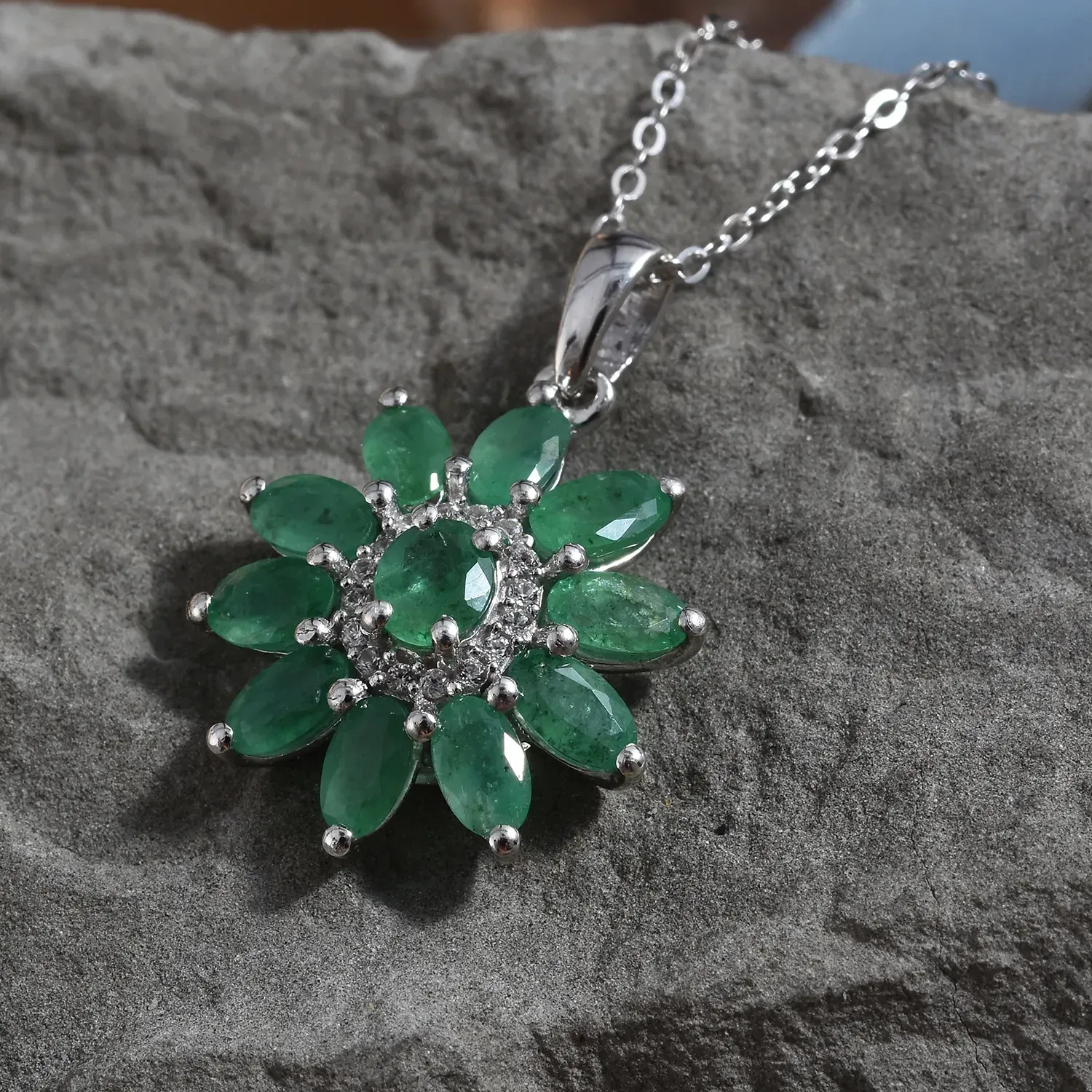 Emerald burst pendant displayed over gray stone background.