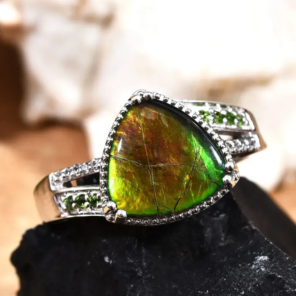 Ammolite ring in silver resting on black stone. 