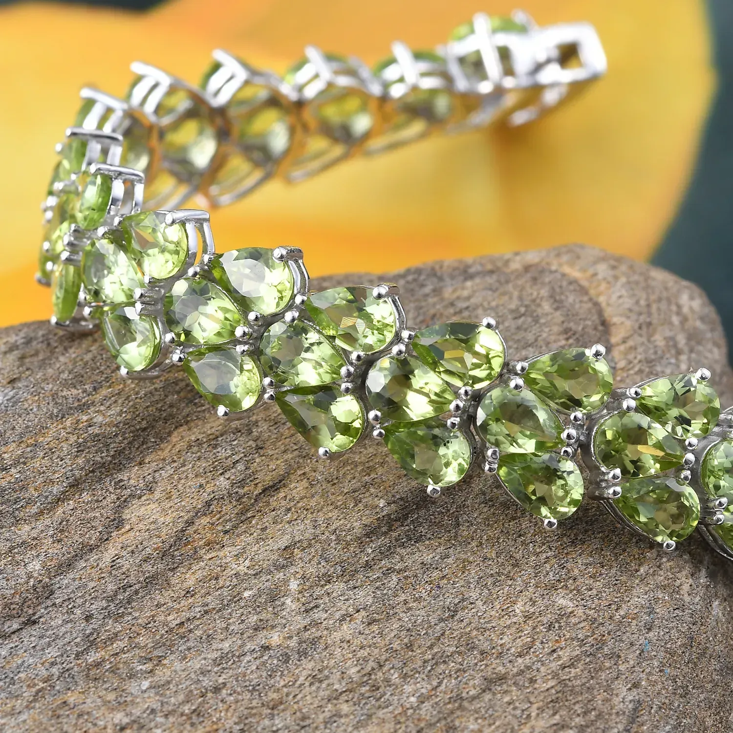Peridot bracelet draped over stone. 