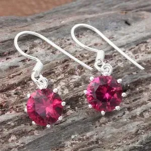Lab created ruby drop earrings draped over wooden display. 