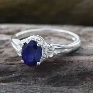 Blue sapphire ring in silver against wood platform.