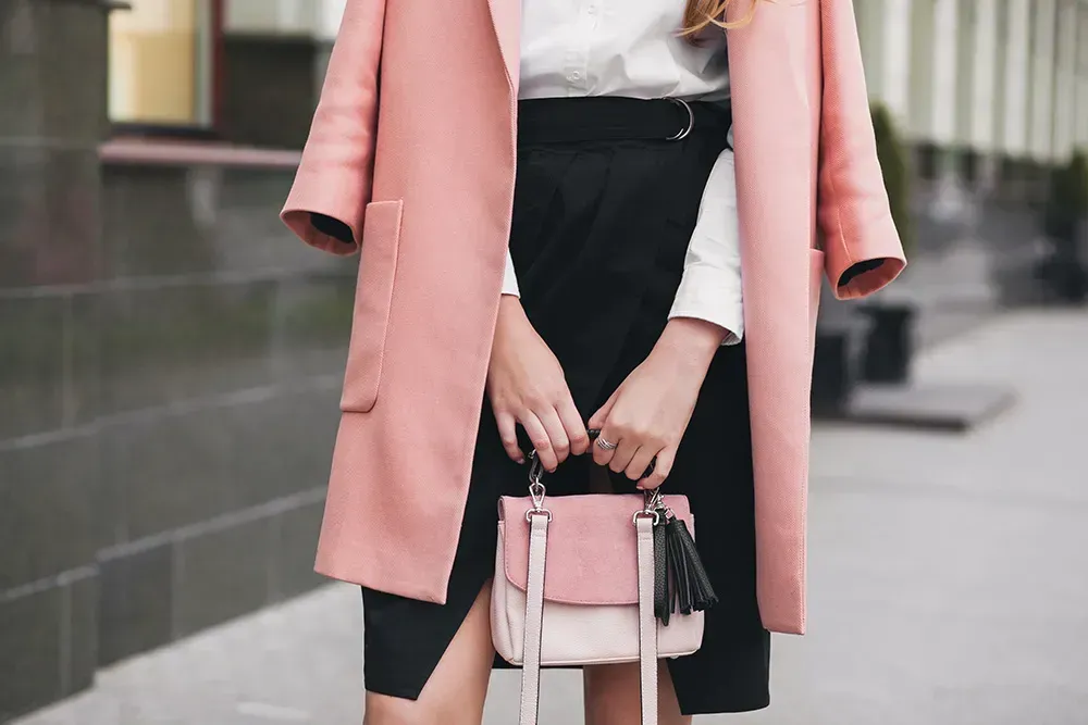 Woman wearing pink blazer and holding a pink purse against black form-fitting skirt