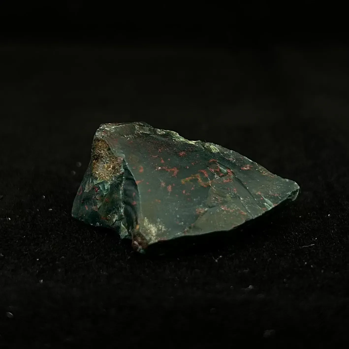 Green bloodstone gem, showing rust red iron oxide flecks. Photographed on a black background.