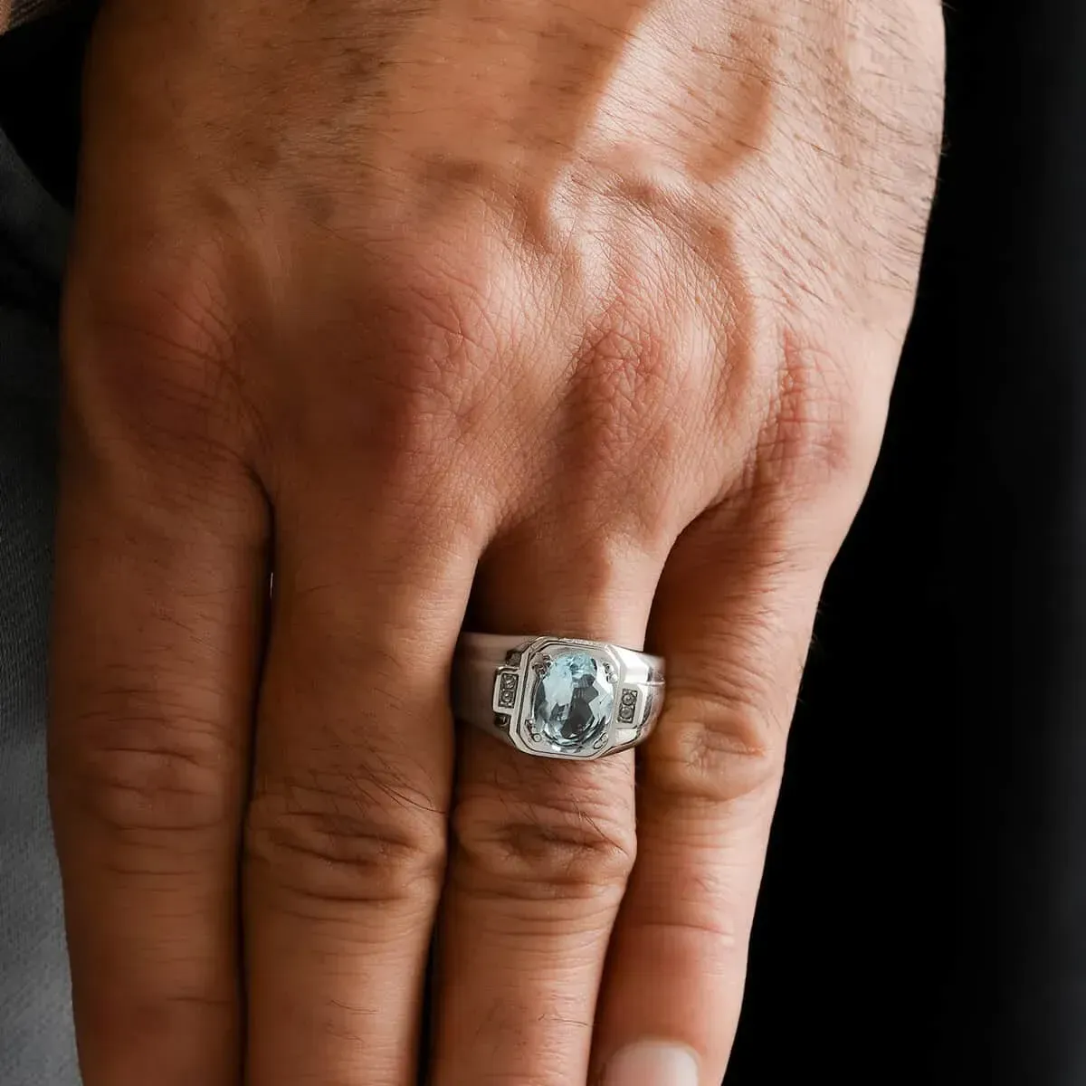 Man's hand modeling a Blue Topaz and White Zircon Men's Ring in Stainless Steel 3.15 ctw against a black background. 