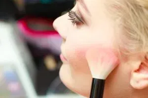 Woman applying blush to her cheek.