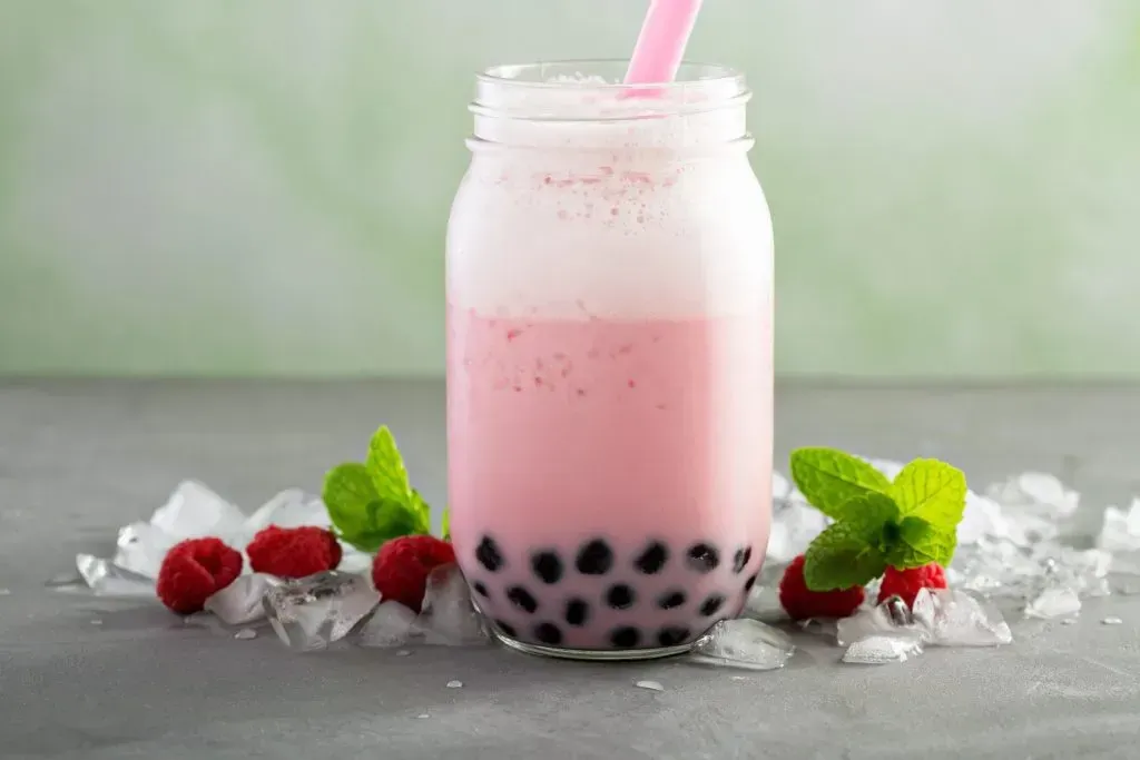 Strawberry pink boba tea in Mason jar glass.
