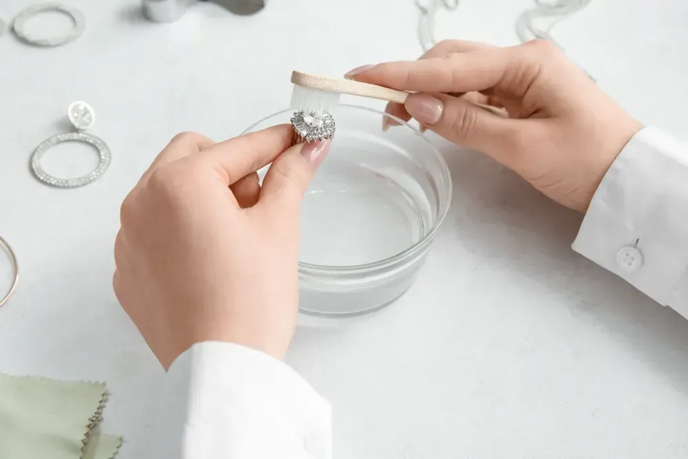 Woman cleaning beautiful ring with toothbrush on light background, closeup