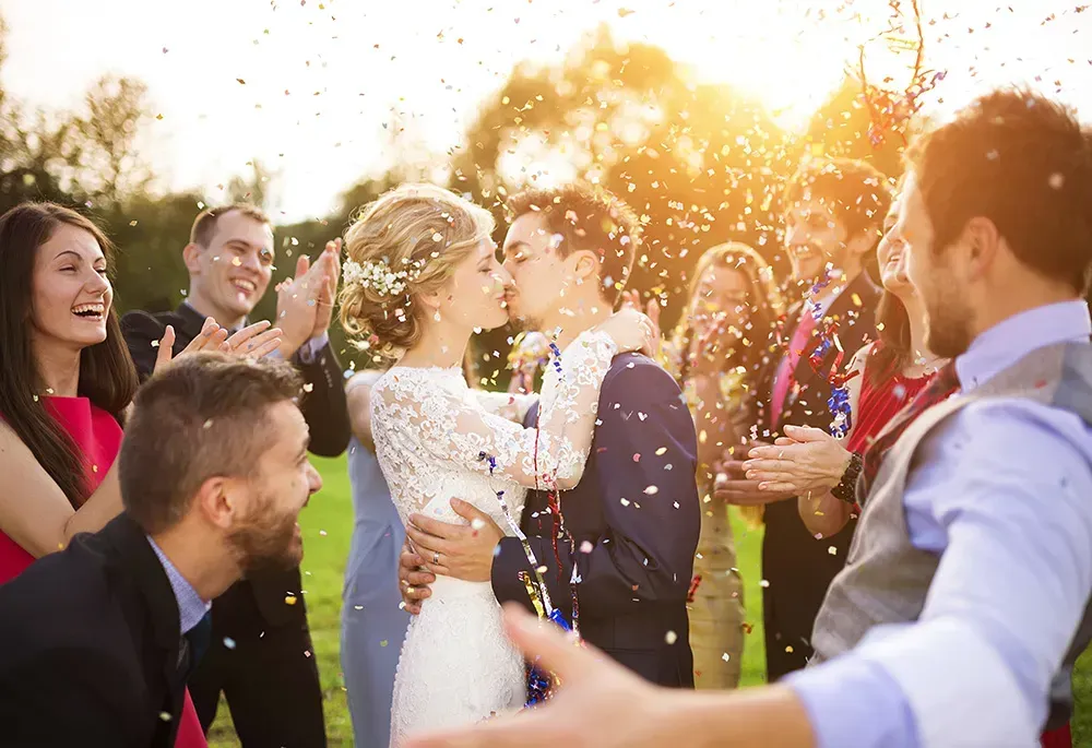 Couple kissing with guests congratulating them.