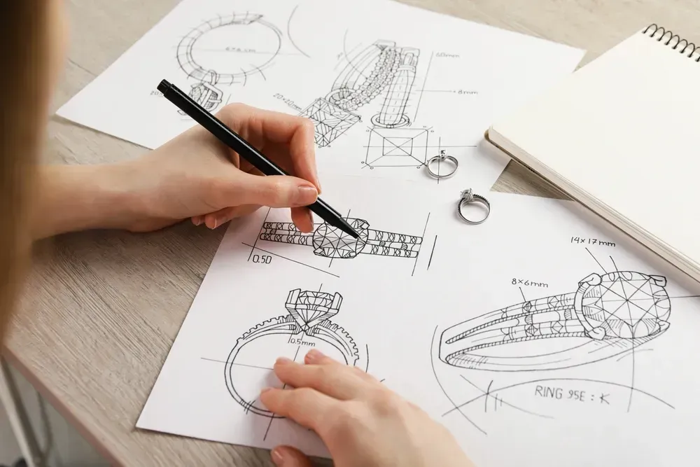 Jeweler drawing sketch of elegant ring on paper at wooden table.