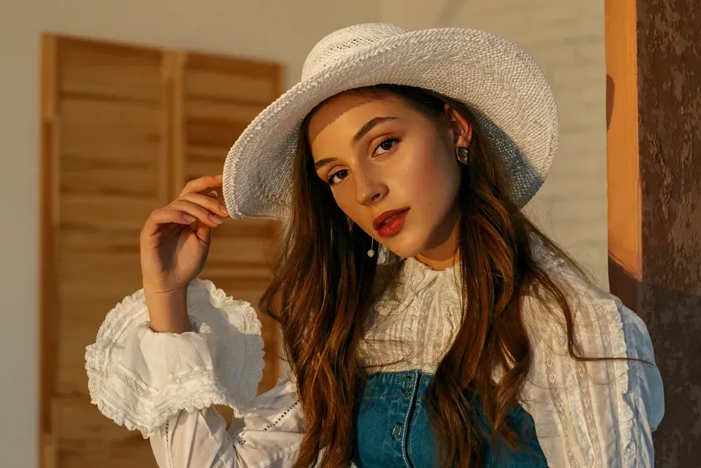 Fashionable woman wearing wicker hat, trendy blue denim corset, vintage style white blouse. Spring, summer fashion concept