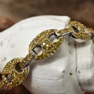 Close up on yellow diamond bracelet draped over shell. 