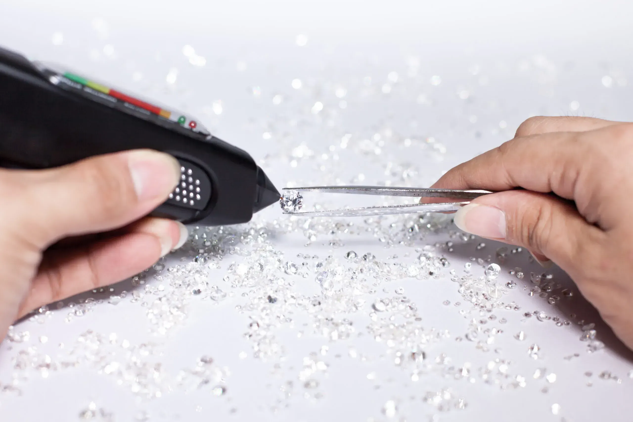 Jewelry holding diamond in tweezers, testing stone with diamond tester. 