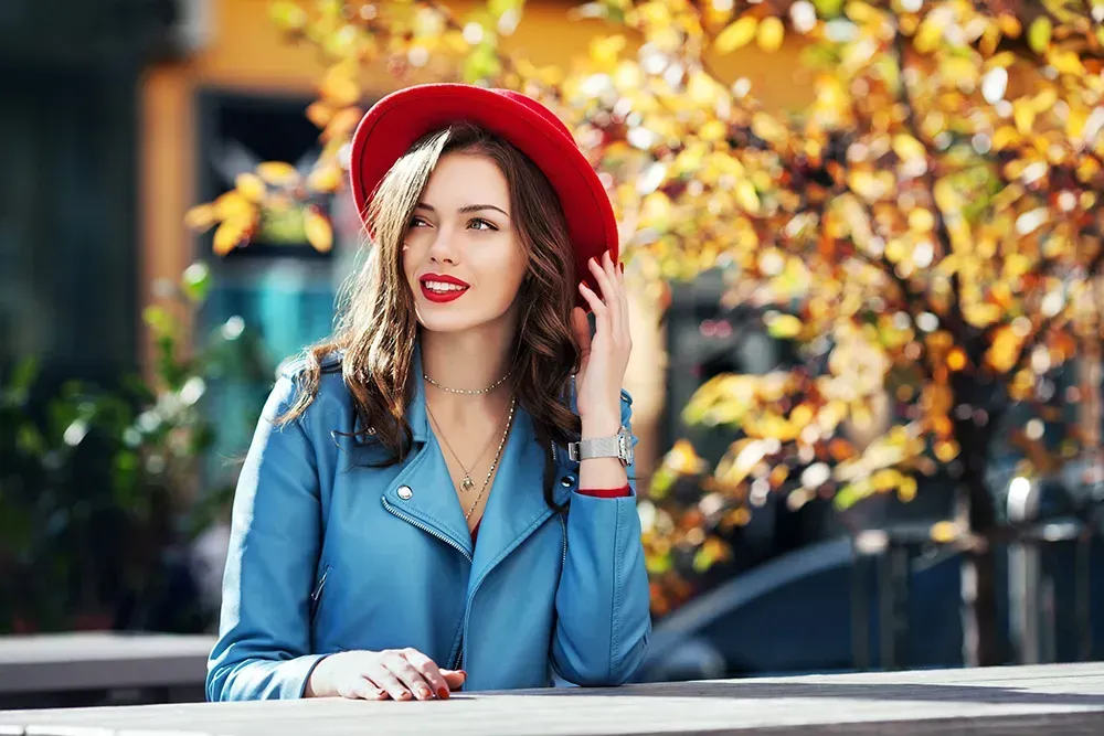 Woman sitting down with denim jacket and a red hat.