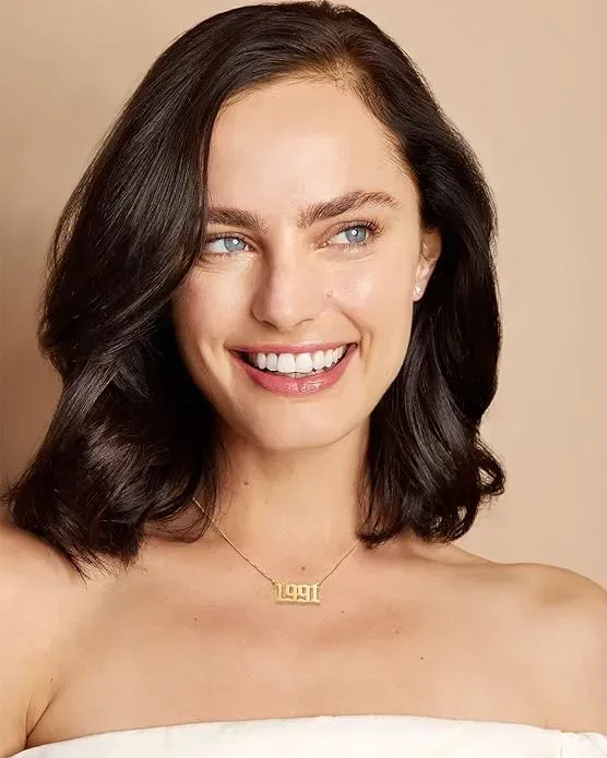 Smiling woman wearing gold plated birth year necklace. 