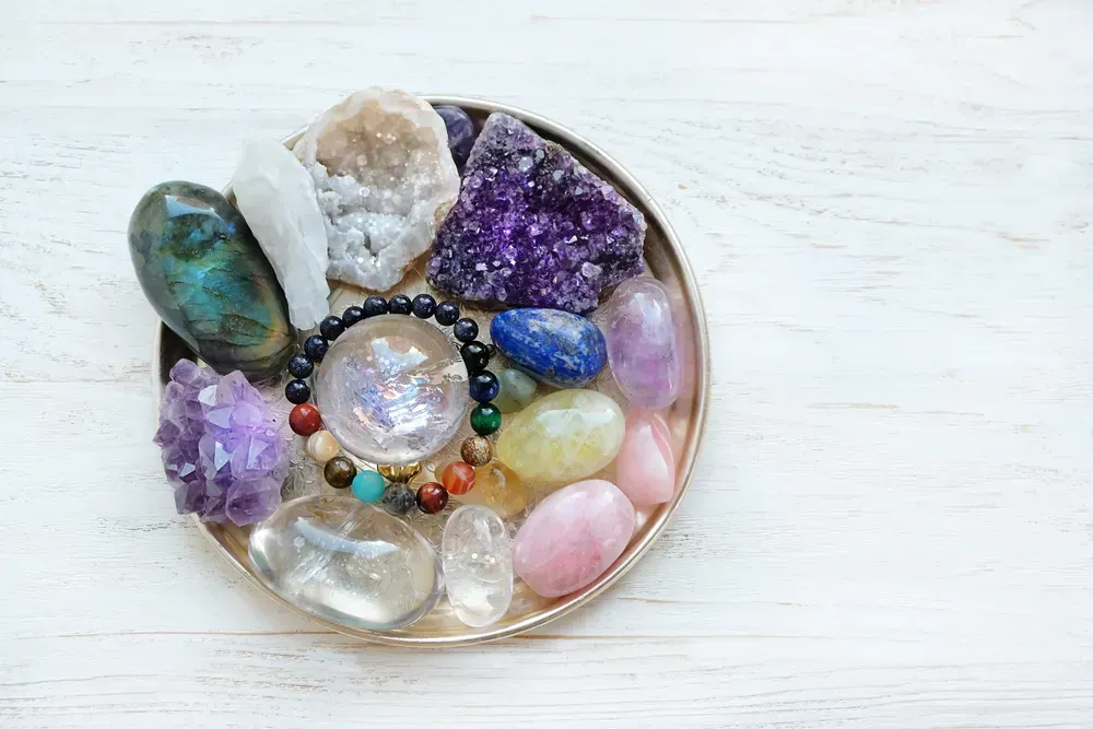 Tray of uncut and polished crystals and a beaded bracelet, in a tray on a light wooden background.