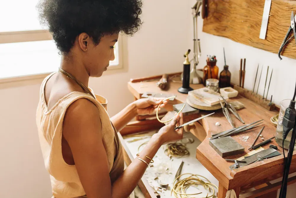 Young woman sitting at workbench making custom jewelry. 