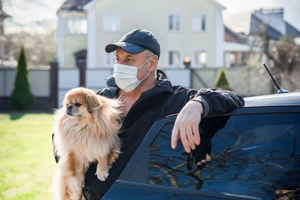 Man in face mask holding dog. 