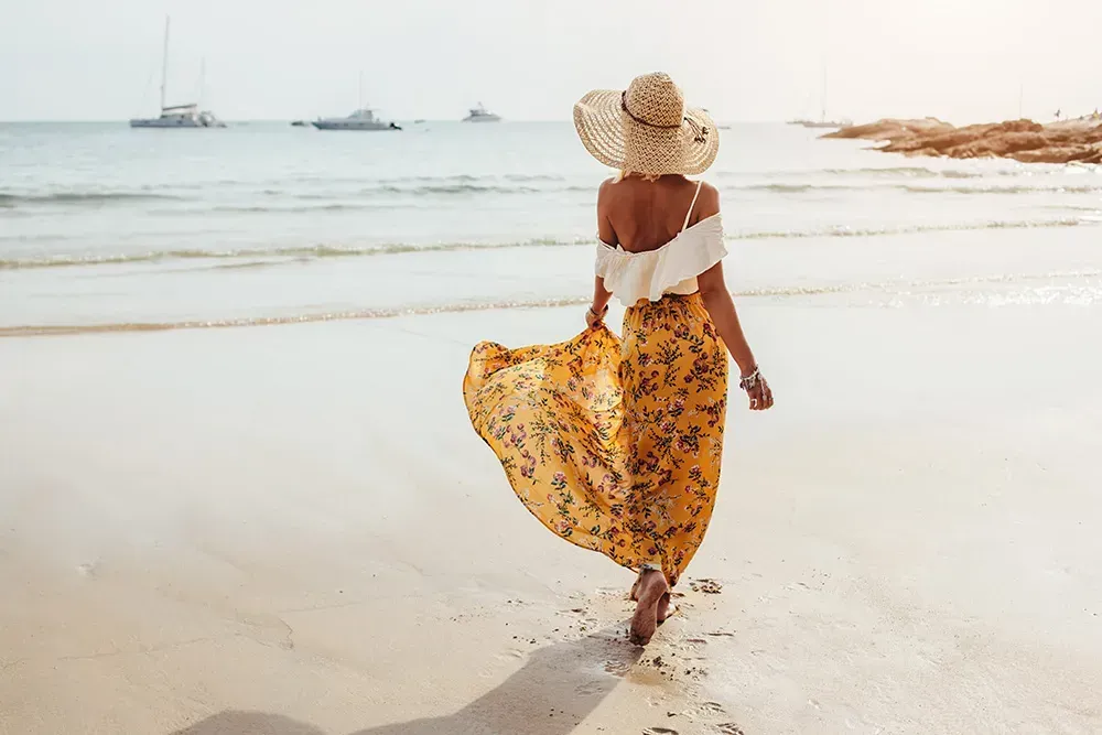 woman facing away from the camera walking in the beach with her maxi dress on