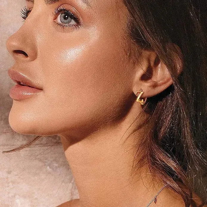 Closeup view of young woman wearing gold initial earrings. 
