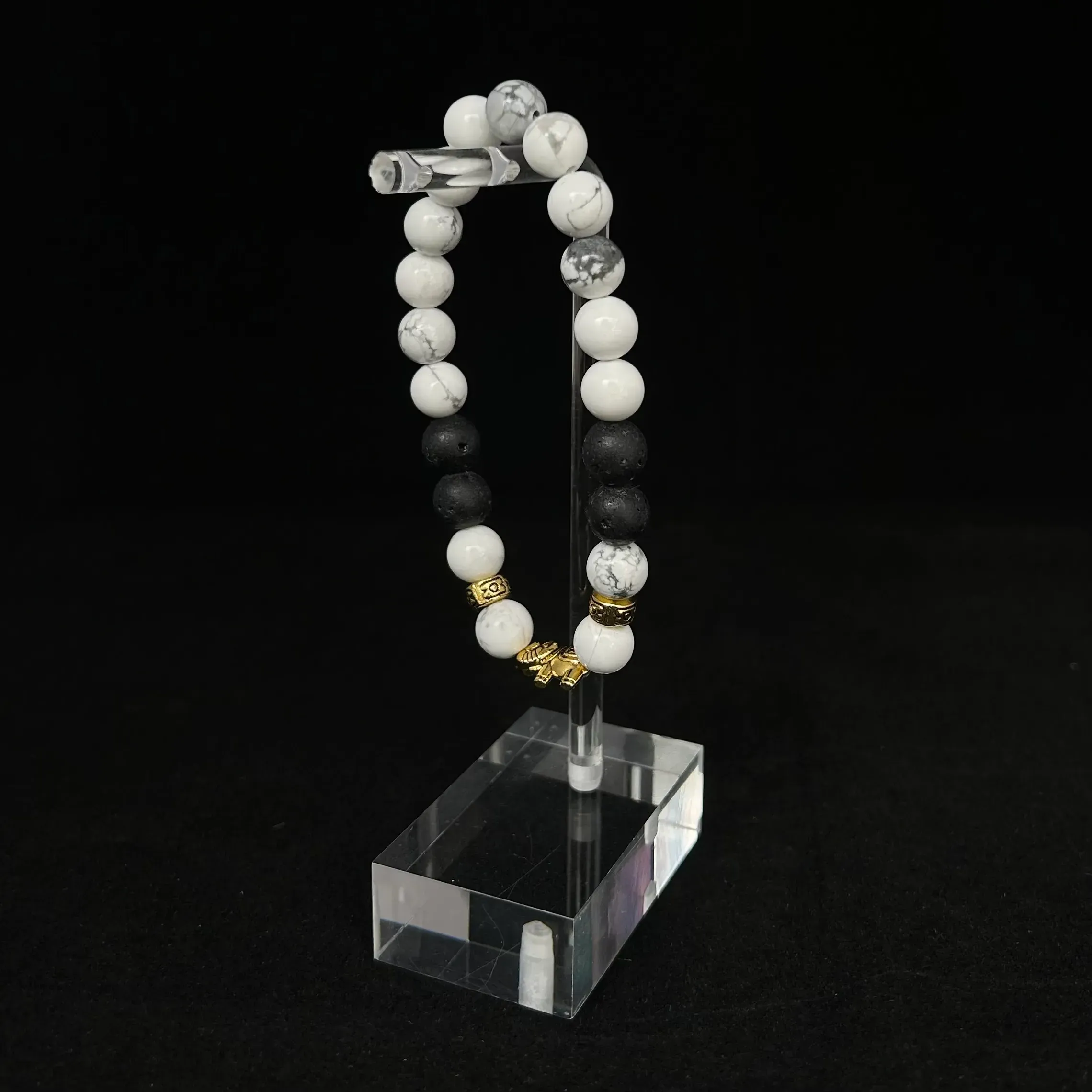 White and black gemstone bracelet on stand against black background.
