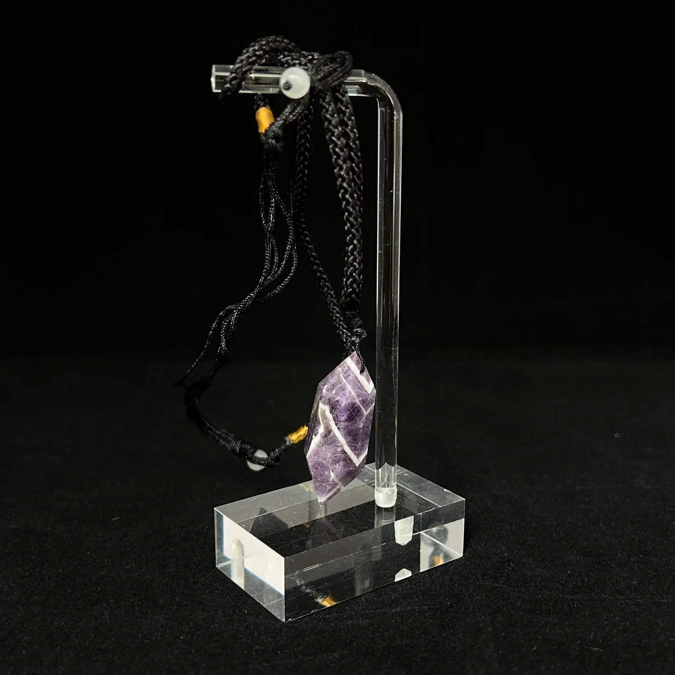 Amethyst pendant on stand against dark background.