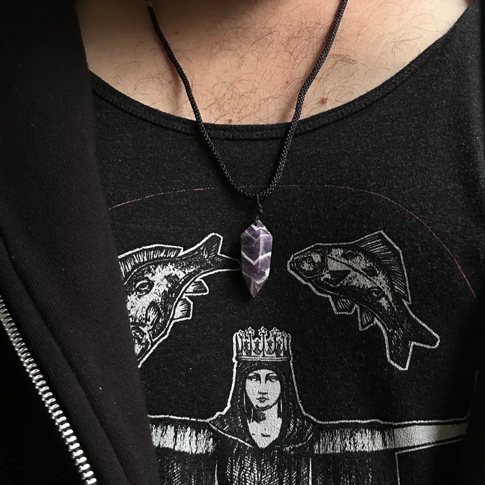 Closeup of man wearing dark clothing and amethyst pendant. 