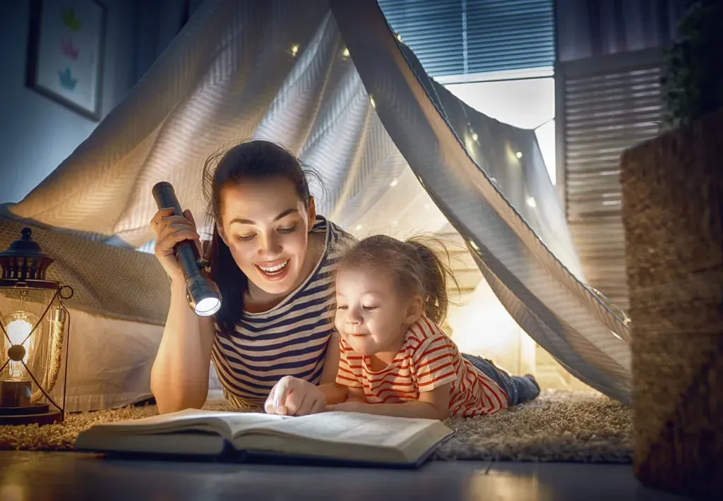Mom and kid reading inside pillow fort.