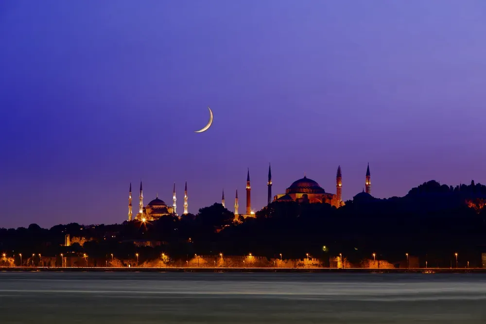 Night view of a mosque and a crescent moon against a violet sky. 
