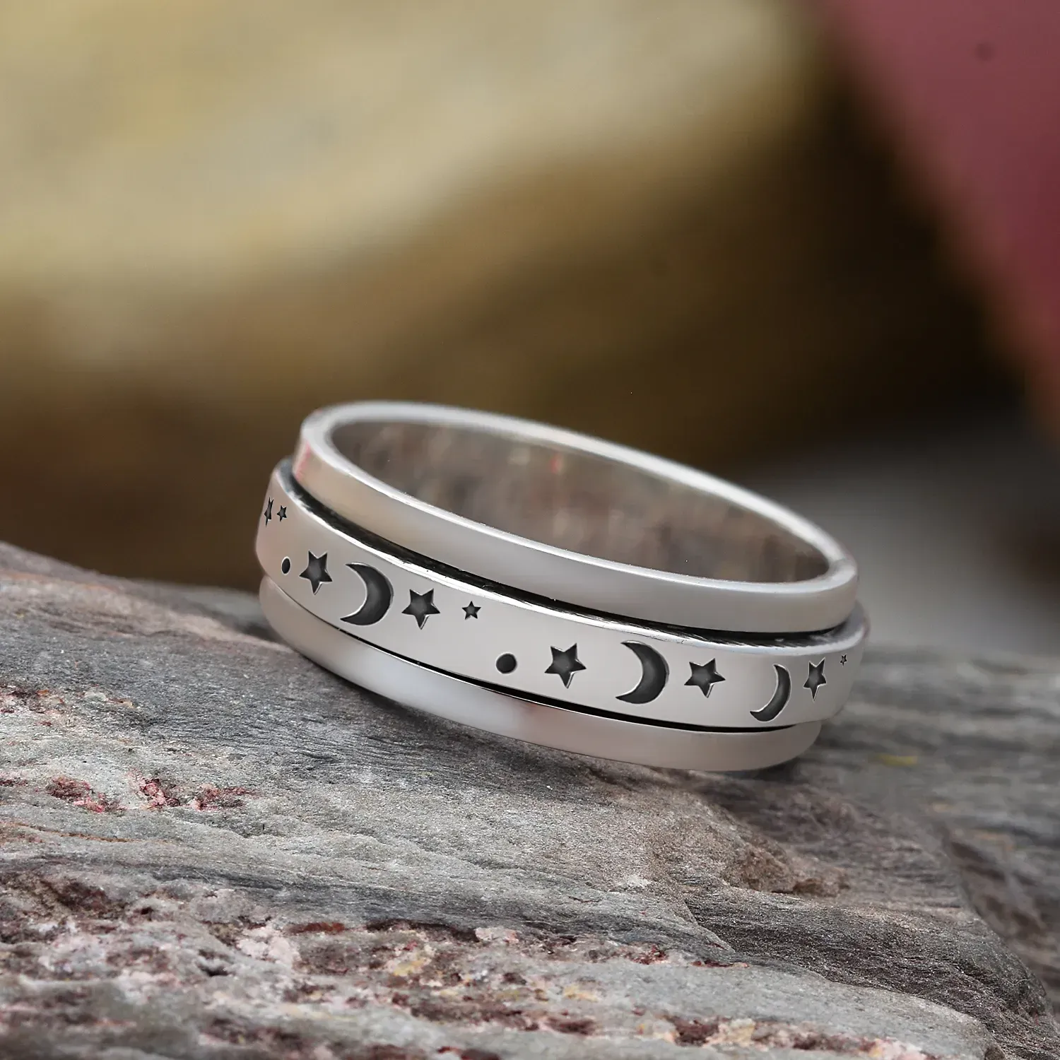 Moon and star spinner ring in sterling silver against a rocky backdrop. 