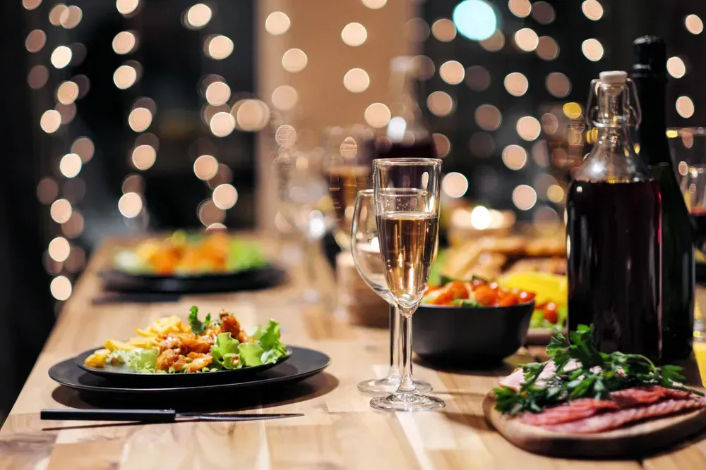 Festive table setting with food and drinks, plates and glasses. Evening lights and candles set the mood for New Year's Eve.