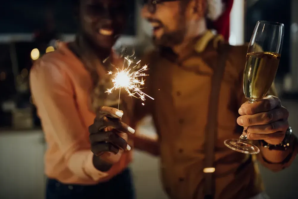 Close-up of a couple celebrating New Year's Eve and having fun with sparklers while drinking champagne at home.