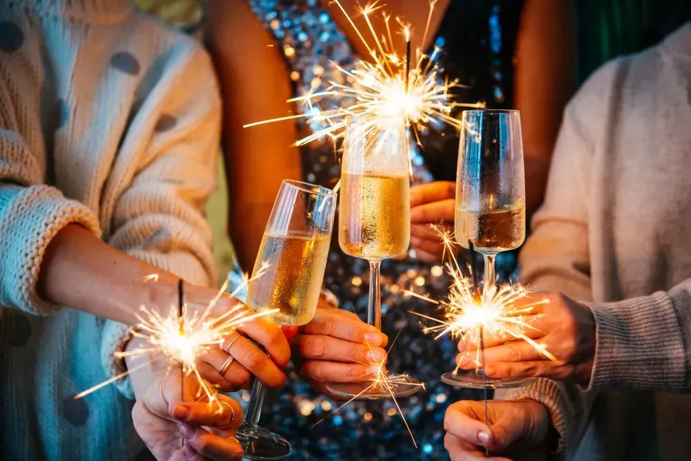 Close up of New Year's Eve part celebrations of hands hold champagne flutes and sparklers. 