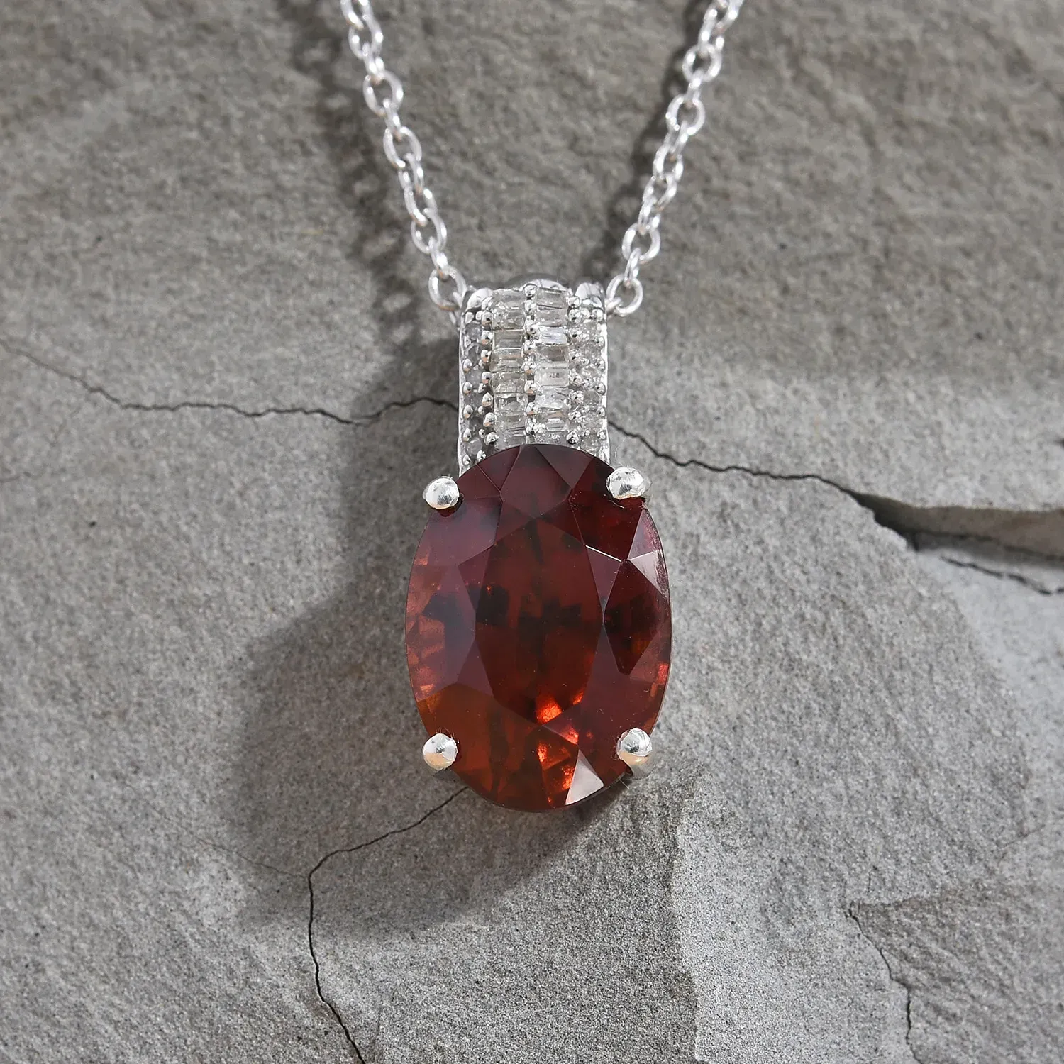 Hessonite garnet pendant resting on gray stone. 