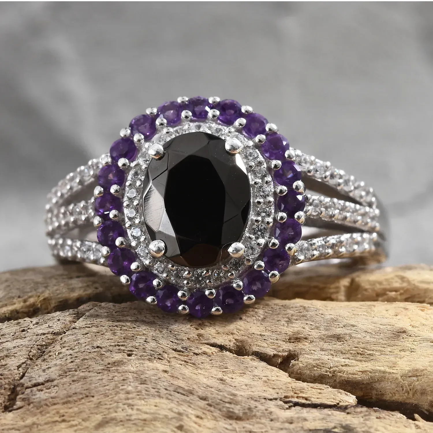 Shungite ring with amethyst halo resting on stone. 