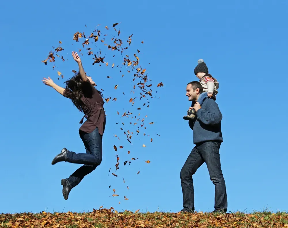 Woman jumping with joy and throwing leaves around her family