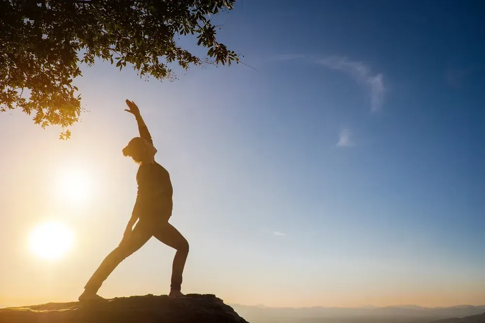 Man doing yoga by a cliff at sunrise