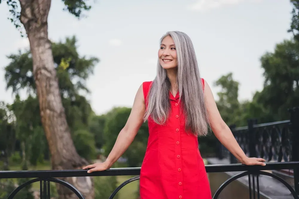 Profile side photo of a mature, attractive asian woman smiling outdoors while wearing a red dress.