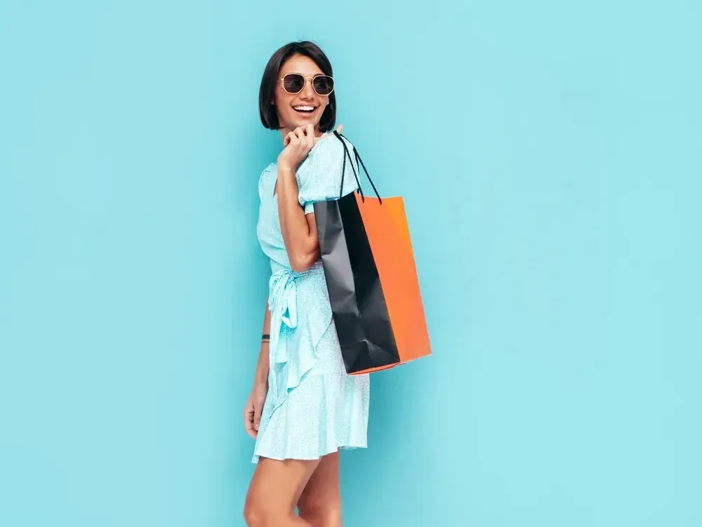 Portrait of young smiling woman in a trendy summer dress holding a shopping bag.