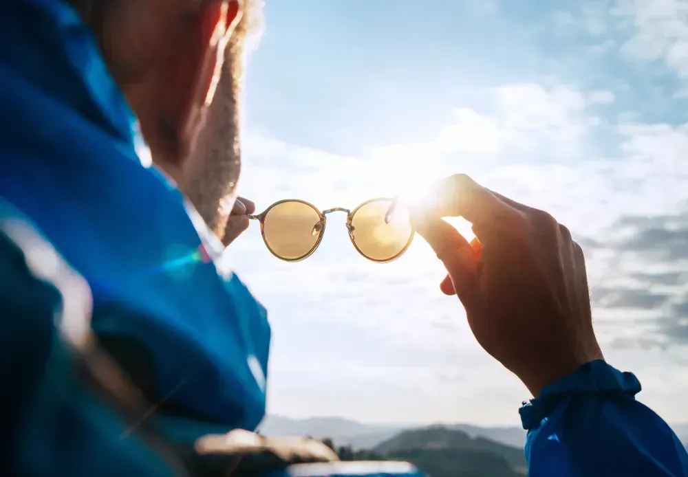 Backpacker looking at bright sun through polarized sunglasses enjoying mountain landscape.